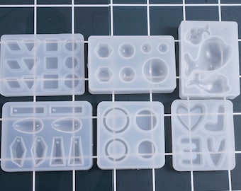 May include: Six clear silicone molds for making resin jewelry. The molds feature various shapes, including geometric shapes, hearts, and a whale.