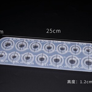 Puede incluir: Un molde de silicona transparente y rectangular con 15 cavidades circulares de diferentes tama&ntilde;os. El molde mide 25 cm de largo, 8,3 cm de ancho y 1,2 cm de grosor. Cada cavidad est&aacute; etiquetada con su di&aacute;metro en cm.