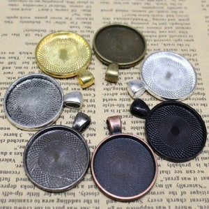 May include: Assortment of eight round metal pendant trays with different finishes, including silver, gold, black, and copper. The trays have a decorative swirl pattern and are designed to hold a variety of materials, such as resin, glass, or fabric.