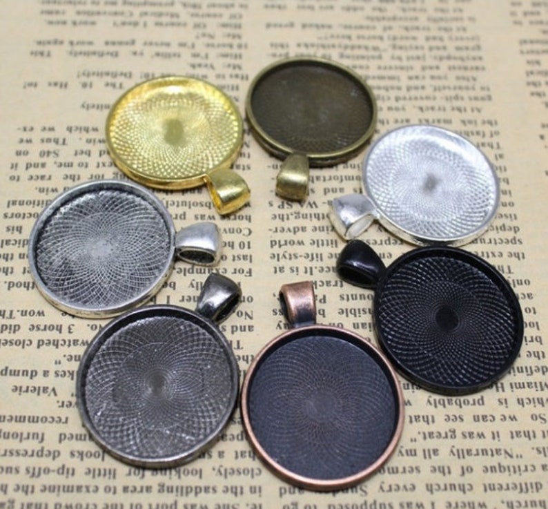 May include: Assortment of eight round metal pendant trays with different finishes, including silver, gold, black, and copper. The trays have a decorative swirl pattern and are designed to hold a variety of materials, such as resin, glass, or fabric.