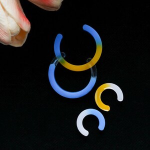 May include: Three hoop earrings in different sizes. The largest hoop is blue and yellow, the medium hoop is blue, and the smallest hoop is yellow.