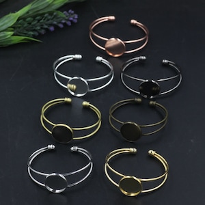 May include: Set of six silver, gold, and copper bangle bracelets with a round, clear glass cabochon in the center of each bracelet.
