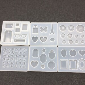 May include: Six clear silicone molds for making jewelry. The molds feature various shapes, including hearts, tags, butterflies, Eiffel Towers, and numbers.
