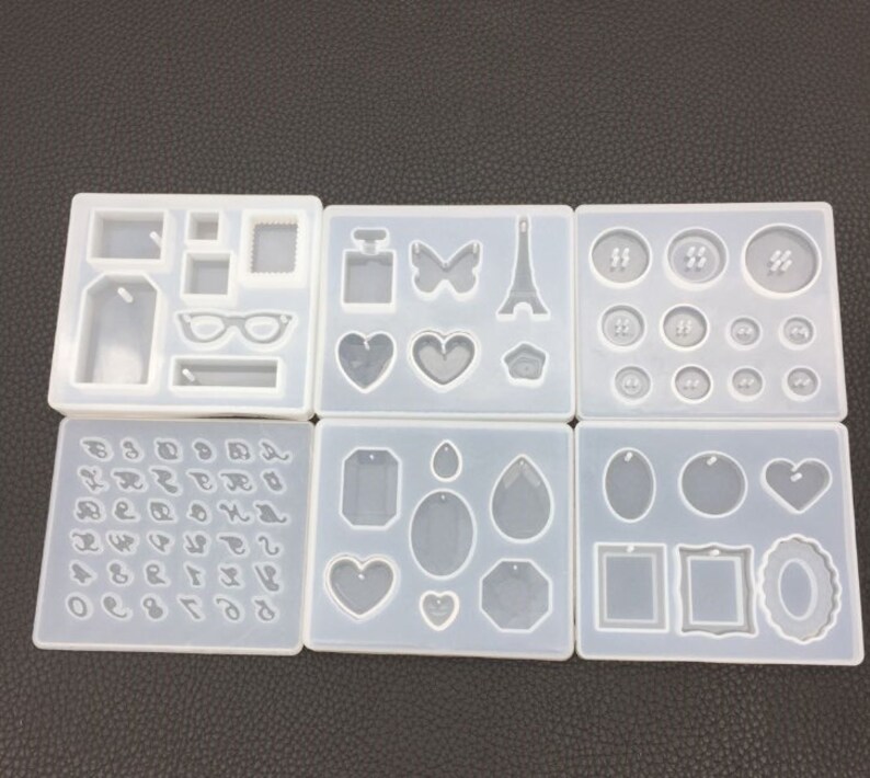 May include: Six clear silicone molds for making jewelry. The molds feature various shapes, including hearts, tags, butterflies, Eiffel Towers, and numbers.