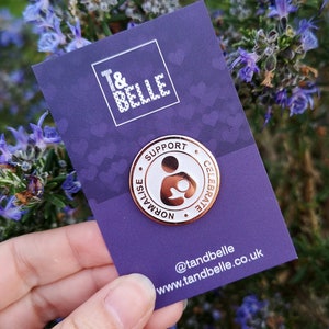 May include: Rose gold pin with a white background. The pin features a silhouette of a person holding a baby. The text around the pin reads "Support, Normalise, Celebrate".