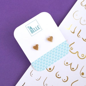 May include: A pair of gold heart-shaped stud earrings on a white card with a blue and white pattern. The card has the text "T&BELLE" printed on it.