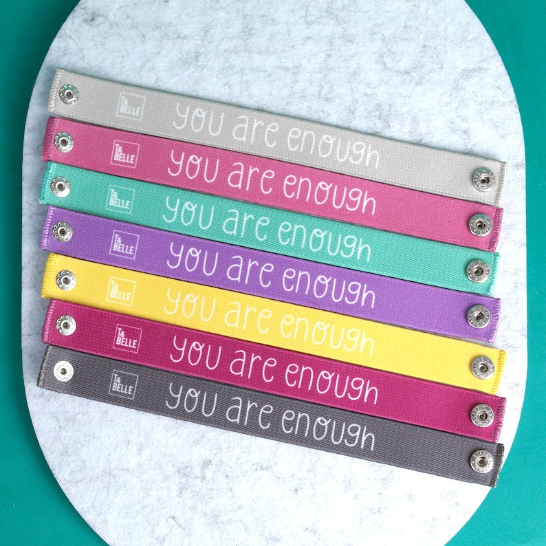 Seven breastfeeding clothing clip wristbands showing the inside edge with the text "You are enough" in white lettering.