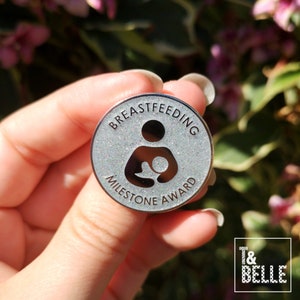 A close up photo of the 6 month 'Silver' Breastfeeding Milestone Award enamel pin, taken outdoors on a sunny day.