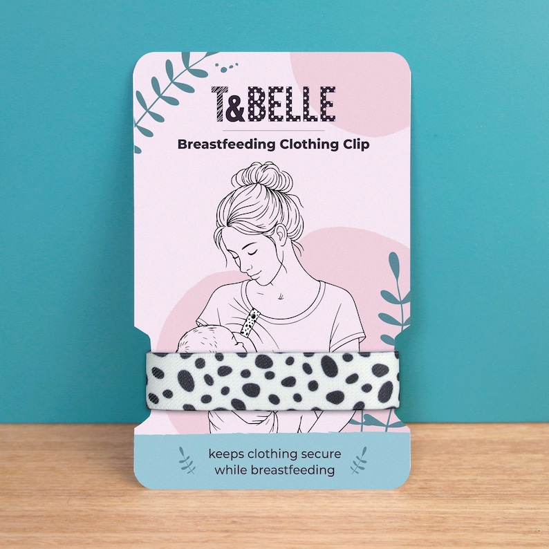 May include: A breastfeeding clothing clip with a black and white polka dot pattern. The product is displayed on a pink and white card with the text "T&BELLE" and "Breastfeeding Clothing Clip". The card features an illustration of a mother breastfeeding her baby.