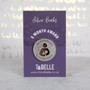 A silver 6 months "Breastfeeding Milestone Award" enamel pin badge with silver glitter on a purple backing card.