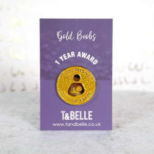 Könnte beinhalten: Eine violette Karte mit dem Text "Gold Boobs 1 Year Award" und eine goldene Glitzernadel mit dem Text "Breastfeeding Milestone Award".