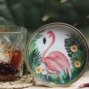 May include: A pink flamingo with green leaves and yellow flowers on a round white plate with a silver rim.