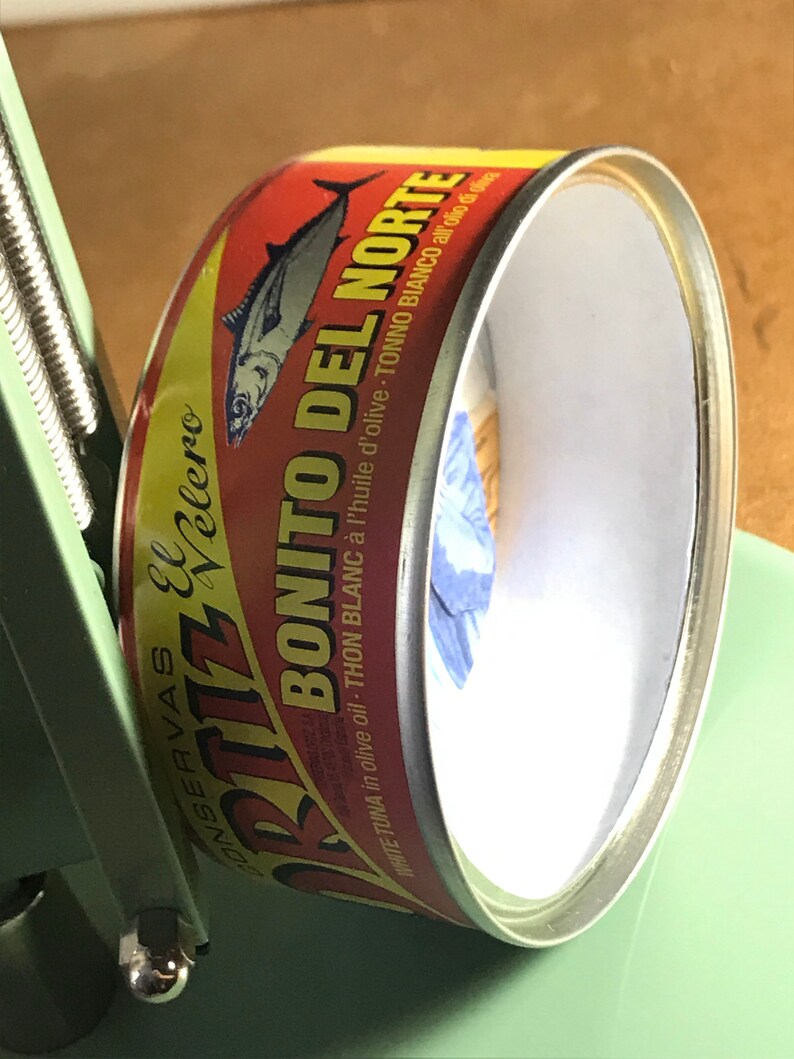 May include: A red, yellow, and white can of Bonito del Norte white tuna in olive oil. The can has a picture of a tuna fish on it. The text on the can reads "Conservas El Velero Bonito del Norte White Tuna in olive oil - Thon Blanc &agrave; l'huile d'olive - Tonno Bianco all'olio di oliva."