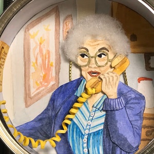 May include: A woman with white hair is on the phone. She is wearing a blue sweater and a striped shirt. The phone cord is yellow and coiled. The background is a watercolor painting of a room.