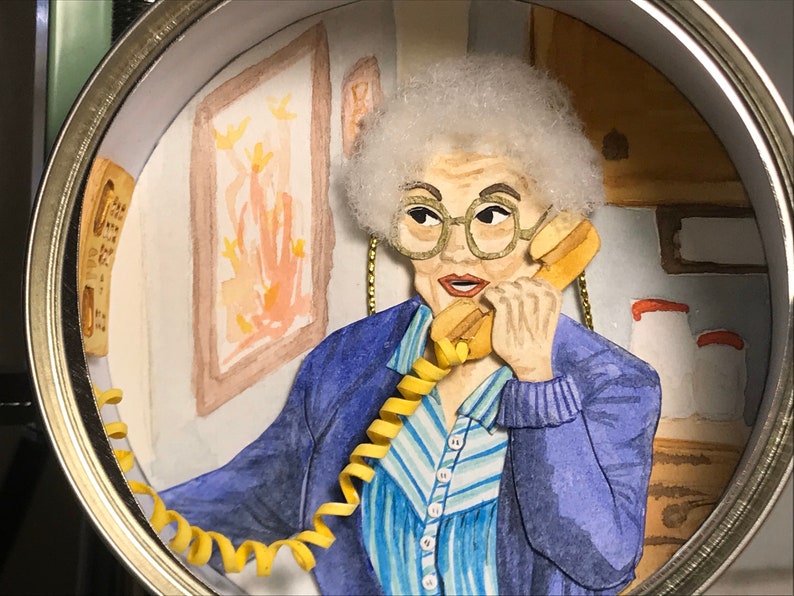 May include: A woman with white hair is on the phone. She is wearing a blue sweater and a striped shirt. The phone cord is yellow and coiled. The background is a watercolor painting of a room.