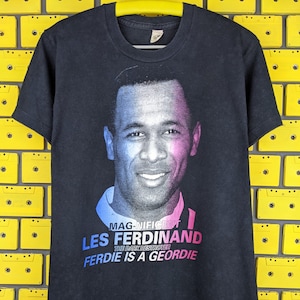 May include: Black t-shirt with a photo of Les Ferdinand, a soccer player, and the text "MAGNIFICENT LES FERDINAND THE DARK DESTROYER FERDIE IS A GEORDIE".