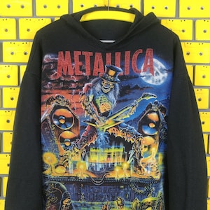 Pode incluir: Camisola de moletom com capuz preta com uma estampa gráfica de um esqueleto tocando guitarra com a palavra "Metallica" em letras vermelhas.