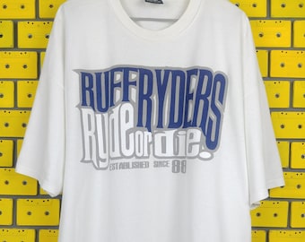Op de afbeelding: Wit T-shirt met een blauwe en grijze grafische print met de tekst "Ruff Ryders Rule or Die! Established Since '88"
