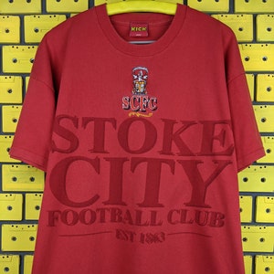 May include: Red t-shirt with a white Stoke City Football Club logo and the text "SCFC" and "EST 1863".