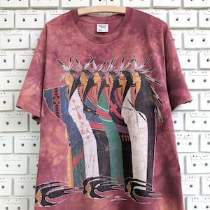 May include: A maroon tie-dye t-shirt featuring a graphic of six Native American figures in traditional attire. The figures are depicted in a row, with detailed clothing in various colors. The shirt has short sleeves and a crew neck.