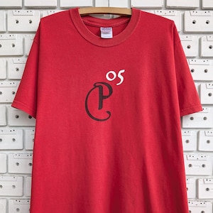 Może przedstawiać: Czerwony T-shirt z czarnym logo "P" i tekstem "os" nad nim.