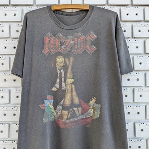 May include: A gray t-shirt with a faded print of a band logo, "AC/DC", and a graphic image of a man and a woman.