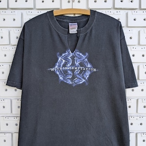 May include: A charcoal gray short-sleeve t-shirt with a notched neckline. The front features a circular blue graphic design with the text "WITHIN TEMPTATION" printed across the center. The shirt has a standard fit and a Gildan brand label.