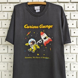 Vintage 00s Curious George camiseta divertido astronauta mono niños libro de aventuras Merch camiseta tamaño XL