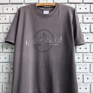 Puede incluir: Una camiseta gris con un gráfico negro de círculo y triángulo y la palabra "PULSAR" impresa en blanco.