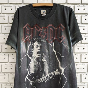 May include: Black t-shirt with a faded image of a rock musician playing a guitar with lightning bolts and the word "AC/DC" in red.