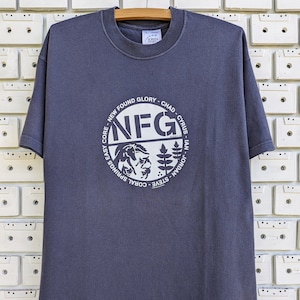 Puede incluir: Una camiseta gris oscuro con un gráfico circular que presenta el texto "NFG" y las palabras "New Found Glory - Chad - Cyrus - Ian - Jordan - Steve - Coral Springs Easy Core".
