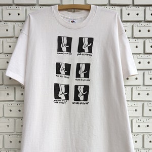 May include: White t-shirt with a black and white illustration of a person's legs in various poses. The text on the shirt reads: "Top shell, to the left", "youre my dreambay", "dve size fits all", "Thanks for your candor", "you must say it", "at lasts all the rest".