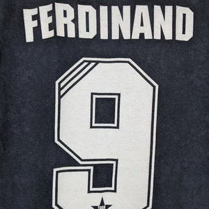 May include: Black t-shirt with white lettering that reads "FERDINAND" and the number "9" in a white block font. A small white star with the text "TOON ARMY" is below the number.