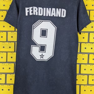 May include: Black t-shirt with the name "FERDINAND" and the number "9" printed on the back. The number is in a white outlined font with a star inside.