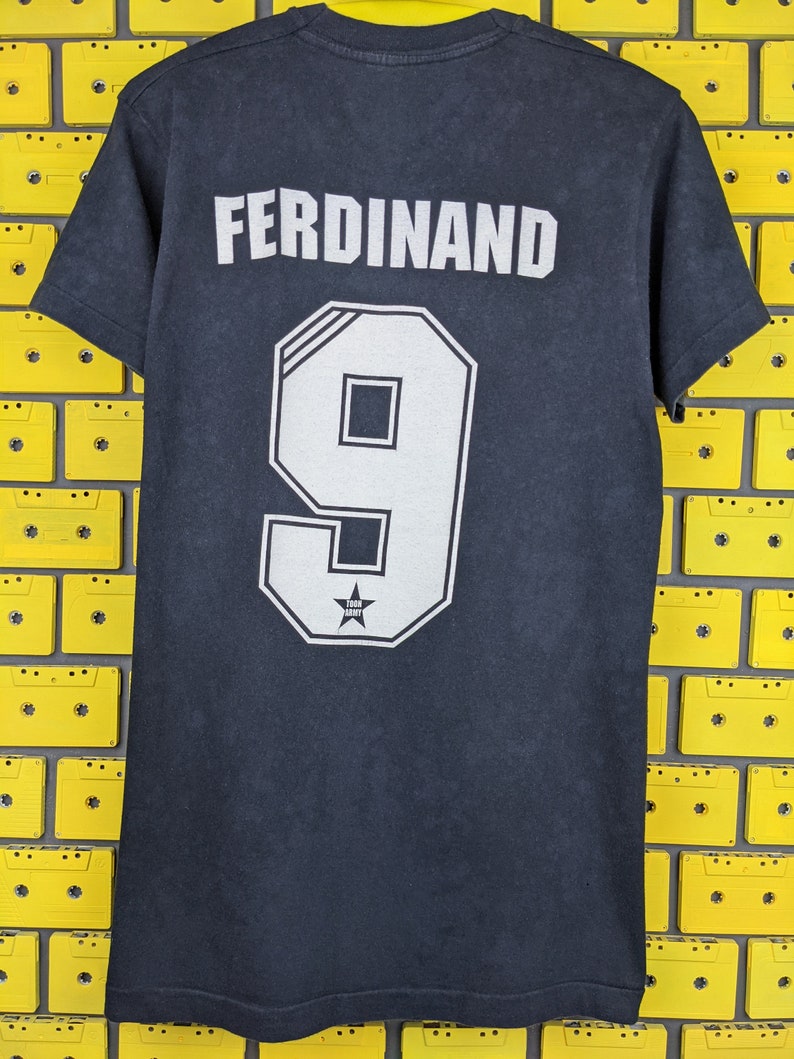 May include: Black t-shirt with the name "FERDINAND" and the number "9" printed on the back. The number is in a white outlined font with a star inside.