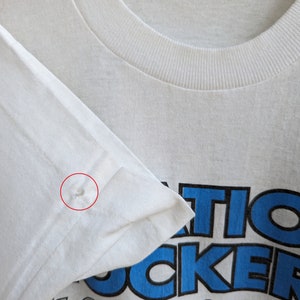 Pu&ograve; includere: Maglietta bianca con una grafica blu e nera che dice "Vacation Sucker" e "It Could Be You" con un piccolo bottone sulla spalla.
