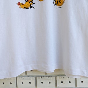 May include: White t-shirt with a cartoon illustration of a group of cats wearing hats and holding a sign that says "It's a cat's life!"