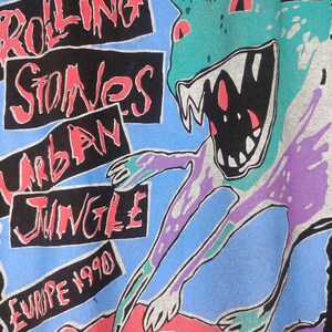 May include: Black t-shirt with a graphic print of a green monster with red eyes and teeth. The text "Rolling Stones Urban Jungle Europe 1990" is printed on the shirt.