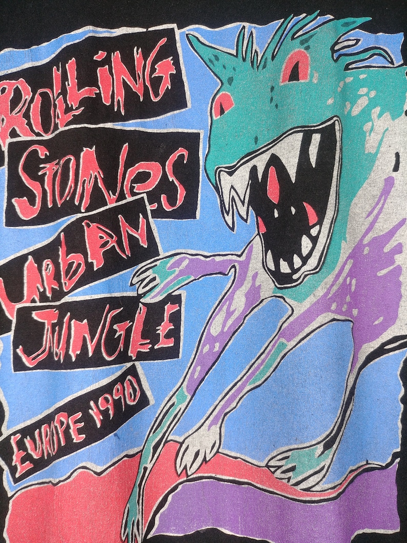 May include: Black t-shirt with a graphic print of a green monster with red eyes and teeth. The text "Rolling Stones Urban Jungle Europe 1990" is printed on the shirt.