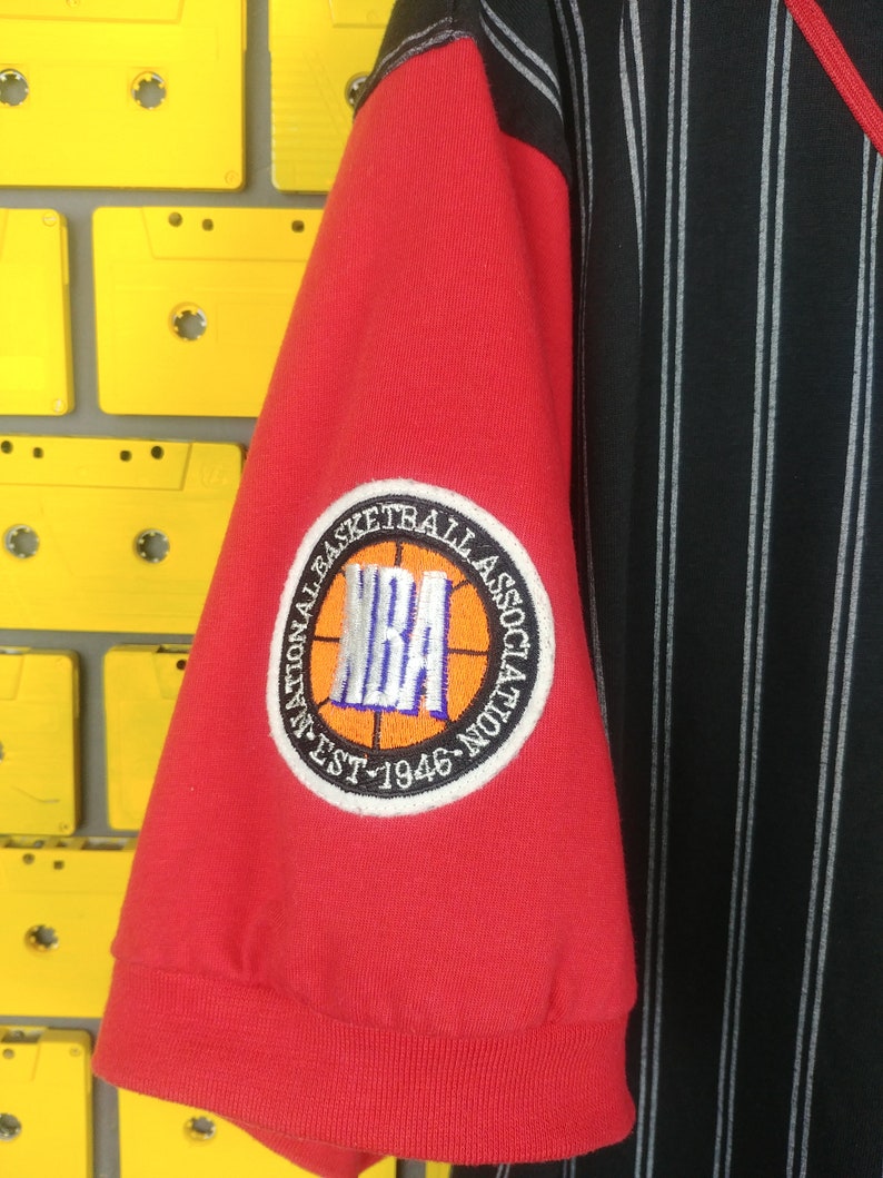 May include: Red and black striped basketball jersey with a red sleeve featuring an embroidered NBA logo patch with the text "National Basketball Association Est. 1946"