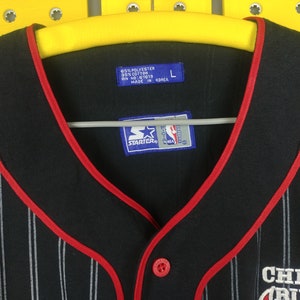 May include: Black and white striped baseball jersey with red trim. The jersey has a red button and a Starter logo with the NBA logo. The text "Chicago Bulls" is embroidered on the front of the jersey.