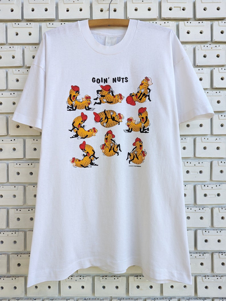 May include: White t-shirt with a graphic of cartoon peanuts in various poses with the text "Goin' Nuts".