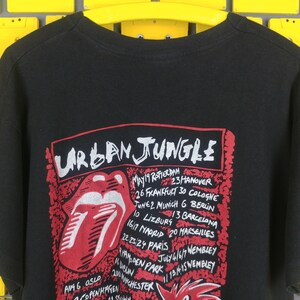 May include: Black t-shirt with a red and white tongue graphic and the text "URBAN JUNGLE" with a list of tour dates and locations.