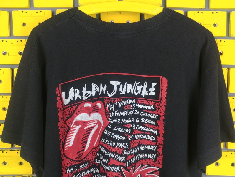 May include: Black t-shirt with a red and white tongue graphic and the text "URBAN JUNGLE" with a list of tour dates and locations.