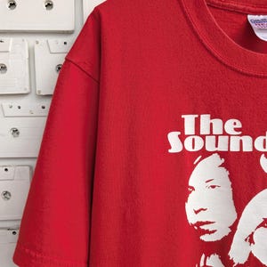 May include: Red t-shirt with a white graphic of the band "The Sound" with four band members' faces.