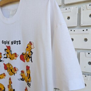 May include: White t-shirt with a graphic of cartoon peanuts in various poses. The text "goin' nuts" is printed at the top of the shirt.
