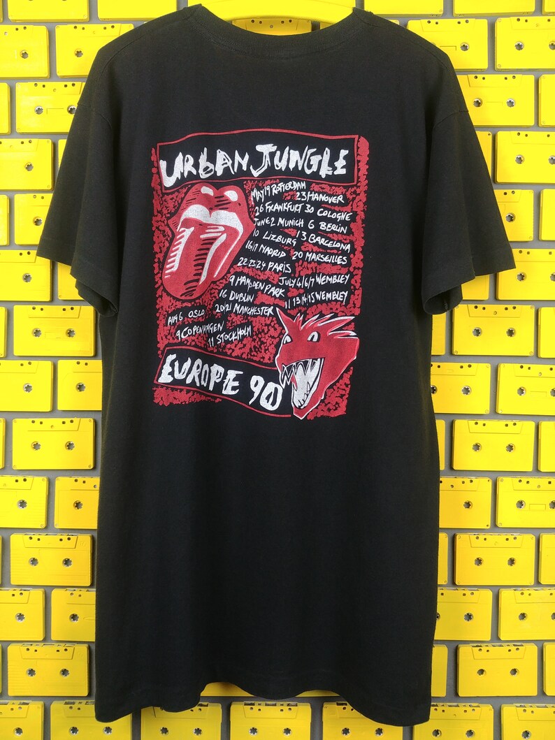 May include: Black t-shirt with a red and white graphic of a tongue and a dragon. The graphic includes the text "Urban Jungle" and a list of European cities and dates. The text "Europe 90" is also included.