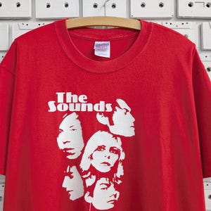 May include: Red t-shirt with a white graphic of the band "The Sounds" and four band members' faces.
