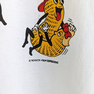May include: A white t-shirt with a cartoon image of a peanut wearing a red baseball cap and sunglasses riding another peanut. The text "MCMXCVI - F&M EXPRESSIONS" is printed below the image.