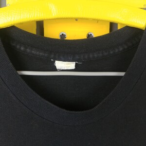 May include: Close-up of the neck of a black t-shirt with a white tag. The tag is blank.